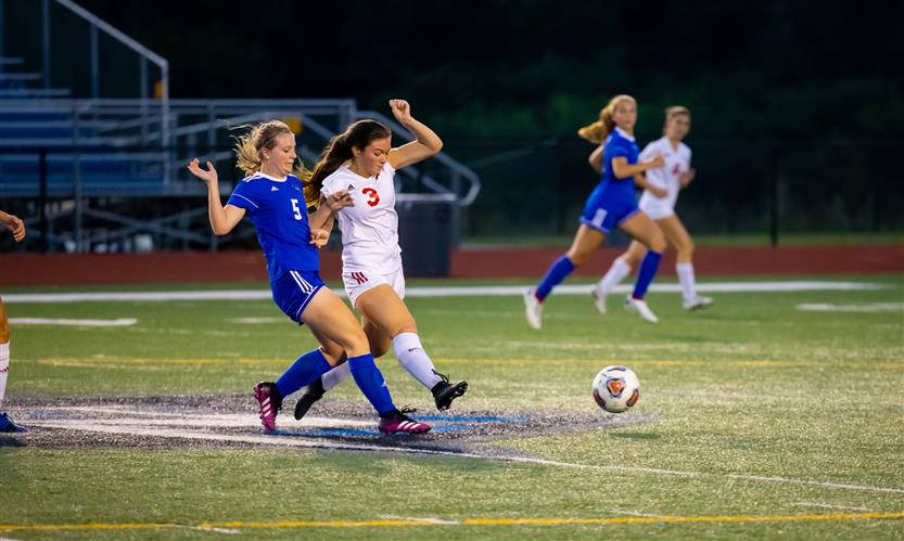 A soccer player runs in between an opponent and the ball